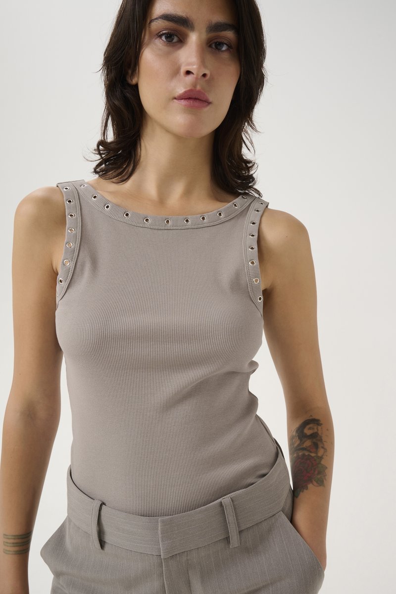 Débardeur beige à côtes avec des détails en œillets le long de l'encolure, associé à un pantalon taille haute à rayures grises.