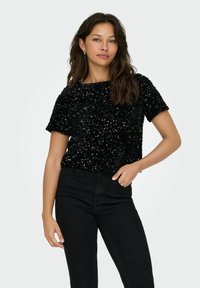 Schwarzes, kurzärmliges Oberteil, das mit Pailletten bedeckt ist, leicht lockere Passform, mit Rundhalsausschnitt und kombiniert mit hoch taillierten schwarzen Jeans.