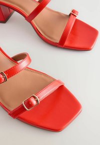 Røde faux læder blokhælede sandaler med to remdesign, firkantede tæer og guldtonede spænder på remmene. Glat beige indersål.