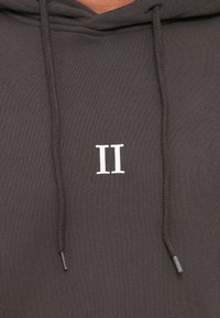 Sweat à capuche gris charbon avec un logo blanc "II", comportant des cordons de serrage et un tissu lisse et texturé.