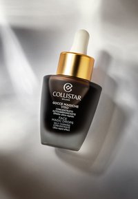 Collistar Face Magic Drops i en mørk glasflaske med en hvid pipette, gylden låg og sort tekst på en lys grå baggrund.