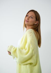 Dzianinowy kardigan w miękkim, przezroczystym, pastelowo-żółtym materiale o luźnym kroju, żebrowanej fakturze i opadających ramionach. Długie rękawy i otwarty przód.