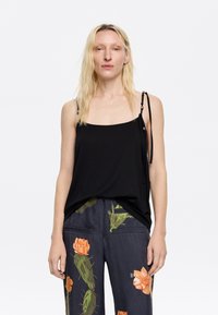 Black camisole with thin straps, featuring a relaxed fit and smooth texture. Paired with navy pants adorned with floral patterns.