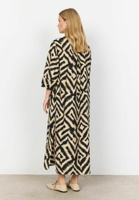 Maxi jurk van lichtgewicht stof met een zwart en beige zigzagpatroon, voorzien van brede mouwen en zijslitsen voor gemakkelijk bewegen.