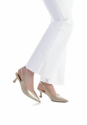 Tacones dorados con tira trasera, punta afilada, acabado texturizado y tacón pequeño y grueso, combinados con vaqueros blancos acampanados.