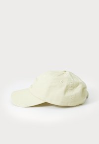 Cream-colored baseball cap with a curved brim, made of soft cotton material. Features ventilation eyelets and adjustable strap at the back.