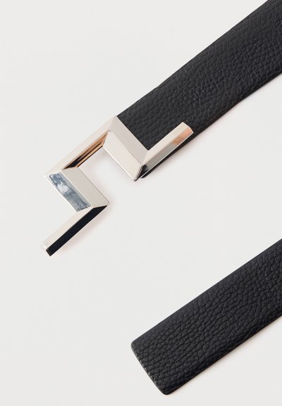 Μαύρη ζώνη από δερμάτινη υφή με γυαλιστερή ασημένια γωνιώδη γεωμετρική αγκράφα σε λευκό φόντο.