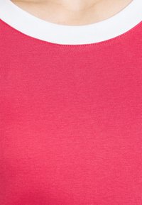 Top aderente in tessuto rosa vivace con texture a costine e colletto tondo bianco. Il materiale è elastico e morbido, adatto per un look informale.