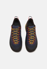 Námornícke modré športové topánky s štruktúrovaným textilným zvrškom, žltými a červenými šnúrkami, čiernou gumovou podrážkou a spevnenou špičkou.