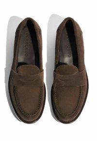 Mocassini in suede marrone con un design cucito, sole piatto e una piccola fascia decorativa sulla parte anteriore. Texture liscia, dettagli minimi.