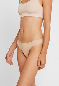 Nude bešavne bikini gaćice izrađene od mekog materijala, s niskim strukom i suptilnim logotipom brenda na elastičnom pojasu.
