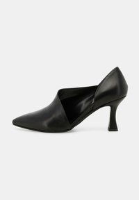 Scarpa nera in pelle con tacco alto, caratterizzata da una punta affilata e un taglio asimmetrico sul lato, con un tacco sottile e angolare.