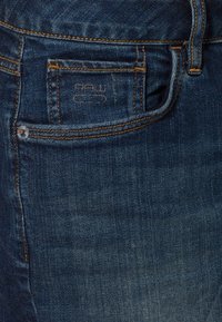 Jeans i mörkblå denim med en urblekt textur. Har en framficka med sömnadsdetaljer och en metallknapp.