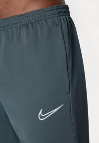 Tmavě šedé sportovní šortky vyrobené z lehkého materiálu s elastickým pasem a bílým logem Nike na levé straně.