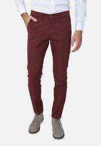 Chino in cotone bordeaux con una vestibilità slim, tasche laterali e chiusura a bottone, abbinati a stivali alla caviglia in suede grigio chiaro.
