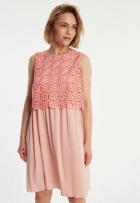 Ein ärmelloses Kleid mit einem strukturierten, bestickten Korallenoberteil mit floralen Mustern, das in einen glatten, hellrosa Stoff darunter übergeht.
