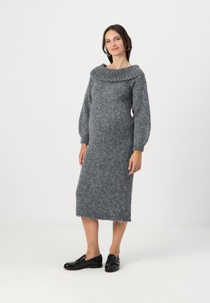 Robe en tricot gris foncé avec un col large à côtes, des manches bouffantes longues et un ourlet au genou. Associée à des mocassins noirs.