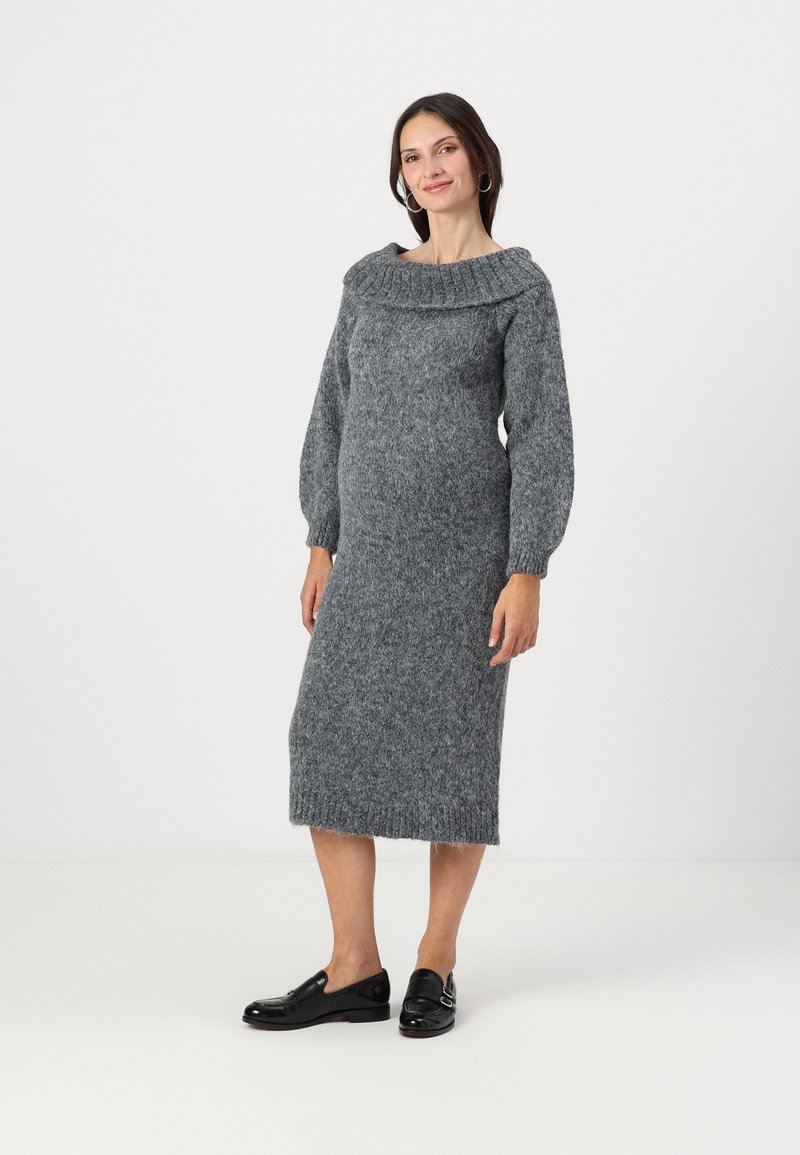 Abito maglione in grigio scuro con scollatura a coste ampia, maniche lunghe a sbuffo e orlo fino al ginocchio. Abbinato a mocassini neri.