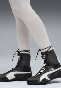 Zwart-witte hoge sneakers met een gestructureerde zool, voorzien van veters en padding rond de kraag. Gemaakt in combinatie met een witte legging.