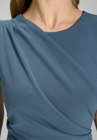 Blauw mouwloos topje van gladde stof, met gedrapeerde details rond de halslijn die een elegante silhoutte creëren.