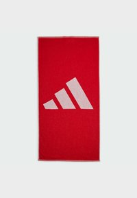 Toalla de felpa roja con un gran diseño de logo de tres rayas en blanco; forma rectangular con una textura suave y un sutil detalle de borde.