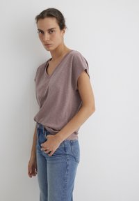 Lila V-Ausschnitt T-Shirt aus weichem Stoff mit umgeschlagenen kurzen Ärmeln, kombiniert mit hoch taillierten hellblauen Jeans. Einfaches, lässiges Design.