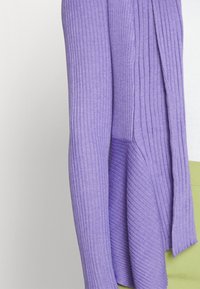 Cardigan côtelé lavande à devant ouvert avec tissu texturé, doté de manches longues et d'une coupe décontractée. Associé à un bas vert.