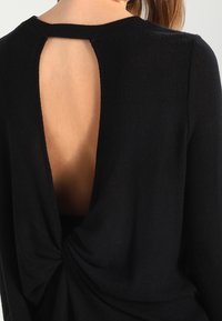 Suéter negro con cuello redondo, que presenta una gran apertura en forma de llave en la parte posterior y un diseño retorcido en la parte inferior de la espalda. Textura suave.