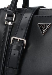Geantă din piele neagră cu o suprafață texturată, având un logo hardware triunghiular de ton argintiu și un brâu reglabil.