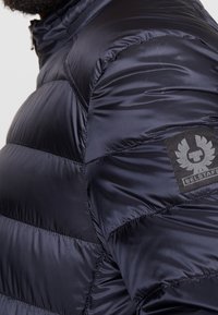 Granatowa pikowana kurtka puchowa z przeszywanymi sekcjami, wykonana z fakturowanej tkaniny, z charakterystyczną czarną naszywką z logo Belstaff na ramieniu.