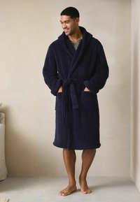 Granatowy szlafrok wykonany z teksturowanej tkaniny w geometryczny wzór, z szerokim kołnierzem, paskiem w talii oraz dwoma przednimi kieszeniami.