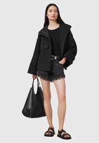 Giacca nera oversize con tasche, canotta nera, shorts di jeans sfilacciati, sandali neri e una grande borsa in pelle nera.