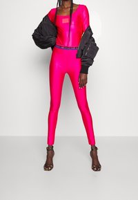 Fuchsia bodysuit met lange mouwen, met een vierkante halslijn. Gepaard met een zwarte bomberjack en sandaaltjes met hakken.
