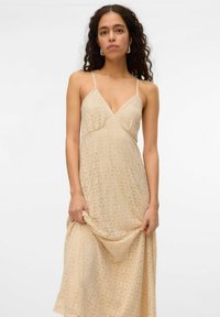 Beige krajková maxi šaty s véčkovým výstřihem, tenkými ramínky a složitým kruhovým vzorem po celé látce. Hladká, splývavá textura.
