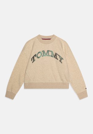 Felpa beige corta con scollo tondo, caratterizzata da un logo testuale "TOMMY" scintillante in paillettes verdi e nere sul davanti.