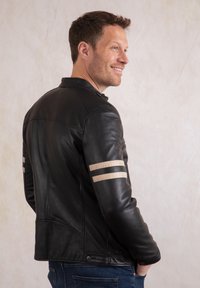 Black leather jacket with a fitted design. Features beige stripes on the sleeves, textured shoulder detail, and a snap closure at the waist.