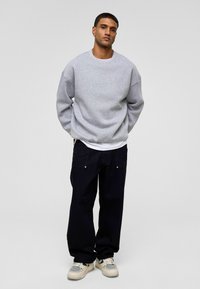 Grijze sweatshirt met een ontspannen pasvorm, gecombineerd met donkere broeken. Sneakers hebben een netontwerp. Effen kleur, geen zichtbare patronen of logo's.