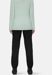 Licht mintgroene top met lange mouwen, met zijnaden en zwarte elastische broek, gecombineerd met zwarte sportschoenen. Minimalistisch ontwerp.