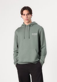 Hooded sweatshirt in muted green, made from soft fabric, featuring a front pocket and white logo text on the chest. Minimalist design.