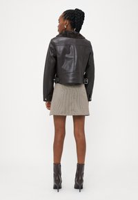 Brun faux læderjakke med pelskant, cropped design, sidelukninger, parret med en beige ternet nederdel og brune ankelstøvler.