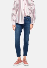 Blue denim skinny jeans with subtle whiskering at the thighs, paired with a white shirt featuring red vertical stripes and text.
