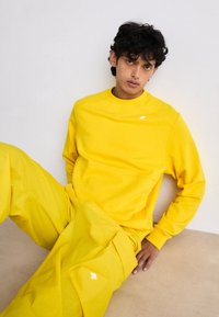 Felpa gialla e pantaloni abbinati realizzati in morbido tessuto. La felpa presenta un logo discreto sul petto; i pantaloni hanno tasche laterali.
