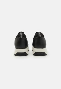 Baskets noires avec une base en cuir lisse, un dessus en maille texturée et une semelle blanche épaisse. Elles comportent un onglet de logo noir et blanc au talon.