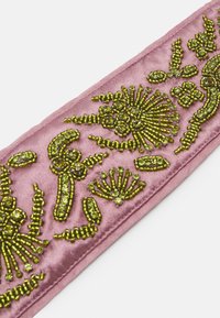 Broderet lyserød satinbånd med indviklede grønne perledesign, der viser blomster mønstre og varierende teksturer.