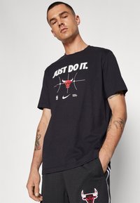 Melnas kokvilnas T-krekls ar uzrakstu "Vienkārši Dari to" baltā krāsā, attēls ar sarkano bulli un NBA logo. Valkāti kopā ar melniem režģa šortiem.
