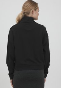 Maglione nero con colletto alto, vestibilità ampia e maniche lunghe. Tessuto testurizzato e polsini a costine ai polsi e all'orlo.