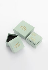 Mintgrüne Geschenkboxen mit goldenen Schriftzügen, wobei eine obere Box geöffnet ist, um ein schwarzes Innenleben zu enthüllen, das elegante, quadratische Designs zeigt.