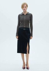 Brun ribbet striktrøje med krave og knaplukning, parret med en sort blyantnederdel med en sidelæg, suppleret med bordeauxfarvede hæle.