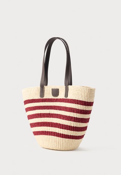Sac cabas en paille tissée avec des rayures horizontales rouges et beiges et des poignées en cuir marron foncé avec des coutures blanches.