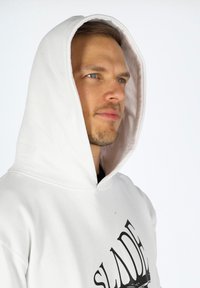 Felpa bianca con una grande grafica frontale che presenta la parola "SLADE." L'interno del cappuccio è di un marrone chiaro a contrasto. Tessuto morbido.